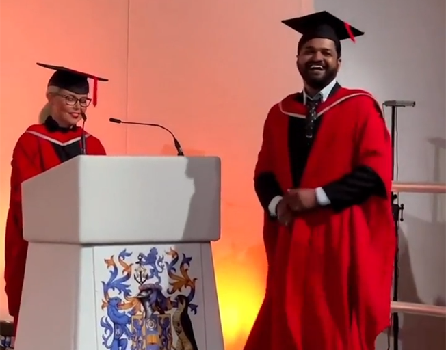 A man on stage about to receive his college diploma